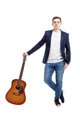 A beautiful guy in jeans and a blue jacket is standing with an acoustic guitar.