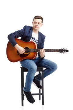 A beautiful guy in jeans and a blue jacket plays an acoustic guitar.