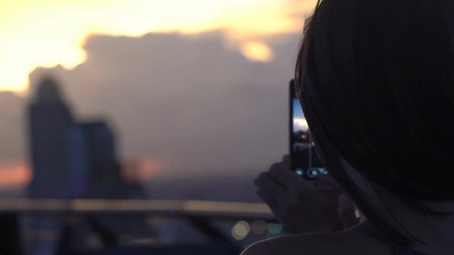 Woman taking photo of sunset with cellphone in skybar, super slow motion 120fps
