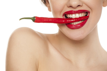 Young sexy woman holding a chili with her teeth on white background