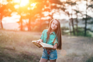 Cute little girl sitting on the grass and reading a book in the