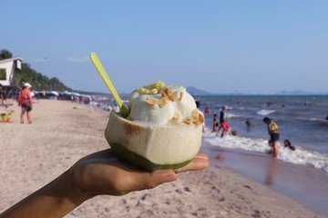 Woman hand holding Ice Cream in a fresh coconut cup Sprinkle with peanuts at the beach In summer Bang Saen.Chonburi, Thailand