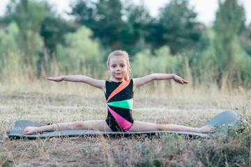 Little cute girl gymnast sits on a splits on mats in the woods