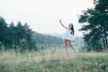 Little cutie girl in a white dress dancing in the woods