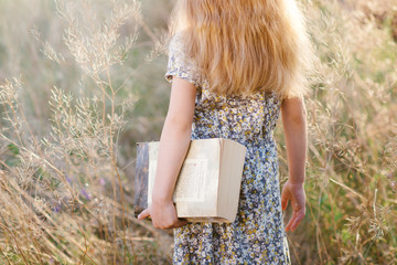 Cute little girl sitting on the grass and reading a book in the