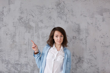 Charming positive girl in casual clothes shows something useful on gray vintage background. Copyspace