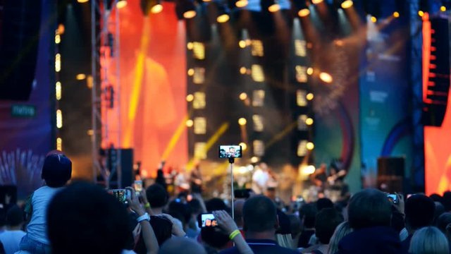 People in crowd making videos with stage of open-air concert on their smartphones. Concept: people, summer, music, festival, concert, crowd