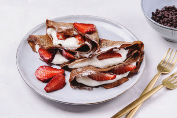 Homemade chocolate crepes with strawberry and cream on grey concrete background. Delicious breakfast. Selective focus