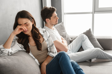 Photo of disappointed couple sitting together on sofa at home with upset look and expressing quarrel, isolated over white background