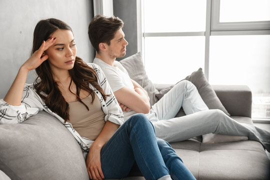 Photo of resentful guy and girl sitting together on couch at home with upset look without conversation, isolated over white background