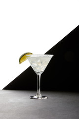Close up view of tasty margarita cocktail with lime and ice on tabletop on black and white backdrop