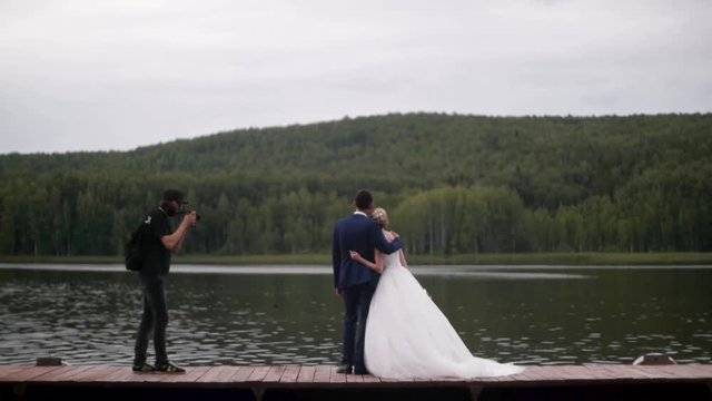 Photographer takes photos of the bride and groom. Clip. Couple. The bride in a white dress and groom on the lake. Rear view on ride and groom on the lake