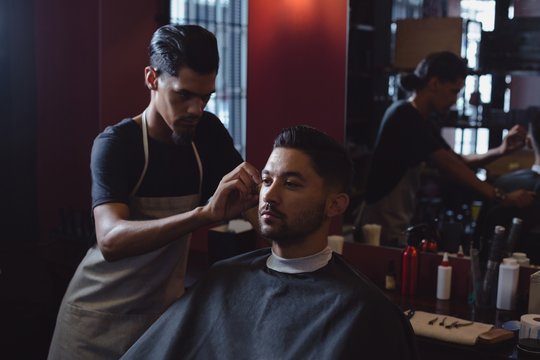 Barber trimming customer hair with scissors in salon