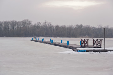 Winter scenery. Timber jetty in frozen river on a foggy winter day.