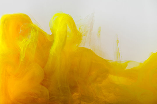close up view of mixing of yellow and brown paints splashes in water isolated on gray