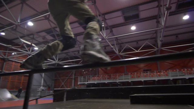A man in an orange sweatshirt performs a grind in a skate park, slow motion
