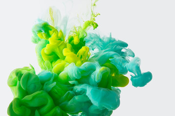 close up view of mixing of green, yellow and bright turquoise paints splashes in water isolated on gray