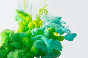 close up view of mixing of green, yellow and bright turquoise paints splashes in water isolated on gray