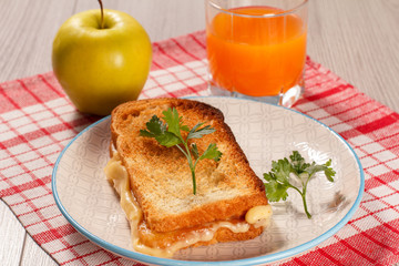 Toast with butter and cheese on white plate, apple and glass of orange juice.