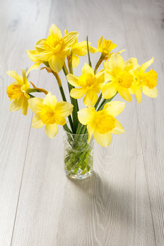 Bouquet of yellow daffodils in vase on wooden desk