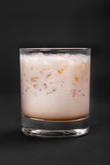 Single-color opaque creamy, milkshake in a low glass, with crushed ice frappe. Side view Isolated black background. Drink for the menu restaurant, bar, cafe