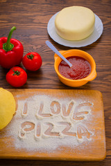 Dough and ingredients for homemade pizza on a wooden background