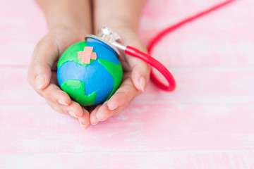 Soft focus of Woman hand holding handmade globe with red Stethoscope on pink pastel wooden table background texture. World Earth Day April 22 and World health day, April 7 concept.