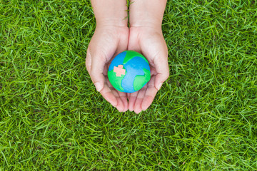 World Earth Day concept. Woman hand holding handmade globe on green grass field background.
