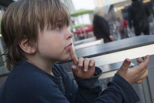 Niño reflexionando sentado en una zona de cafés y  ambiente urbano de ciudad.