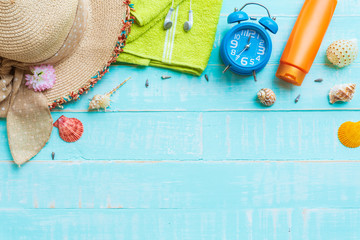 Beach accessories including sunglasses, sunscreen, hat beach, shell, alarm clock, green towel and Earphone on bright blue pastel wooden background for summer holiday and vacation concept.
