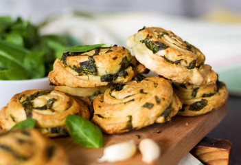 Buns of puff pastry with spinach and garlic close-up on a wooden board against a background of a bowl of spinach. Homemade pastries with greens.