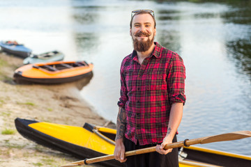 handsome man holding paddle and standing near kayaks on riverside