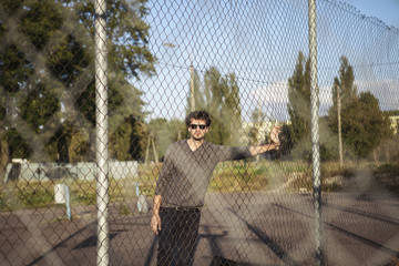 Handsome man in sunglasses leaning on iron fence and posing on camera