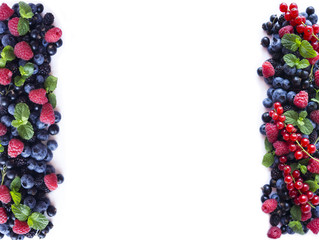 Mix berries and fruits at border of image with copy space for text. Ripe blueberries, blackberries, black currants and raspberries on white background. Top view.