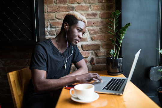 Handsome afro american man sitting at cafe listening music and looking at laptop