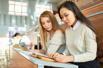 Fototapeta premium Two beautiful girls studying notes sitting at desk in lecture hall of modern college, copy space