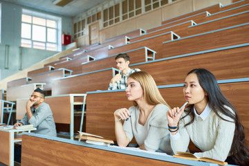 International group of people sitting at separate tables in lecture hall of modern college...