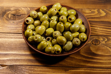 Plate with green olives on wooden table