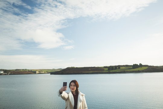 Woman taking selfie with mobile phone near riverside
