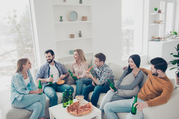 Cheerful, stylish, attractive, positive community sitting in living room, house having snacks on the table looking at each other spending free time together enjoying weekend