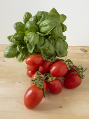 group of red pachino tomatoes on wooden table with bunch of fresh green basil