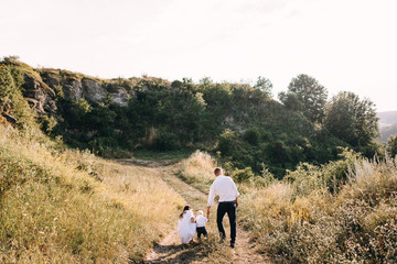Fototapeta na wymiar Walk beautiful young family in white clothes with a young son blond in mountainous areas with tall grass at sunset. Mother keeps son in her arms, hugging. family - this is happiness