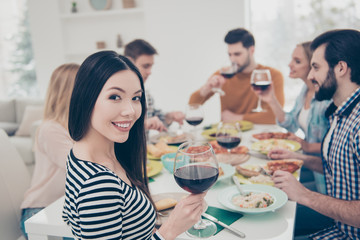 Charming, stylish, brunette girl sitting at the table with her best friends celebrating birthday looking at camera holding glass with red wine guests, visitors enjoying delicious, tasty, meals, dishes
