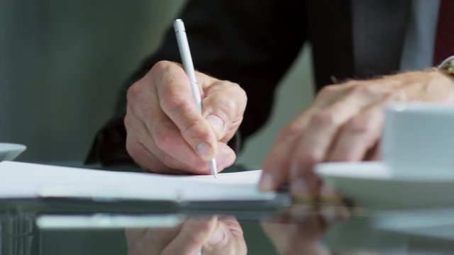 Tracking closeup shot of hands of businessman sitting at table and signing contract