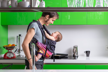 Young man making breakfast with his baby in carrier