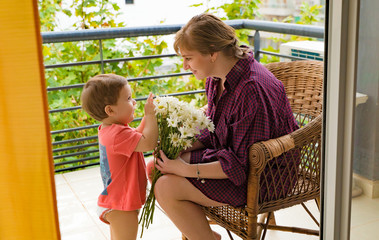 happy grandmother with grandson and a bouquet of camomiles on the balcony