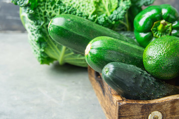 Tray with Fresh Organic Green Vegetables Savoy Cabbage Zucchini Cucumbers Bell Peppers Avocados on Black Stone Concrete Kitchen Table by Window. Rustic Style Superfoods Vegan Plant Based Diet Concept