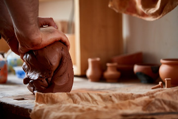 Hands of male potter molding a clay in pottery workshop, close-up, selective focus