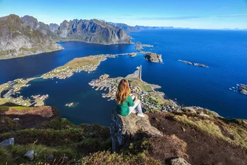 Fototapete Rund The red hair girl is sitting on the top of Mount Reinebringen on Moskenesoy with a view of the Reine, Hamnoy, Vest fjord and Flakstadoy on the Lofoten Islands beyond the Arctic circle in Nordic Norway © Мария Белоусова