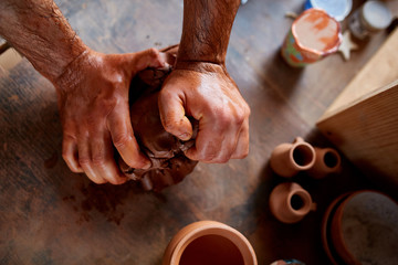 Male potter molding a clay in pottery workshop, close-up, selective focus, top view.